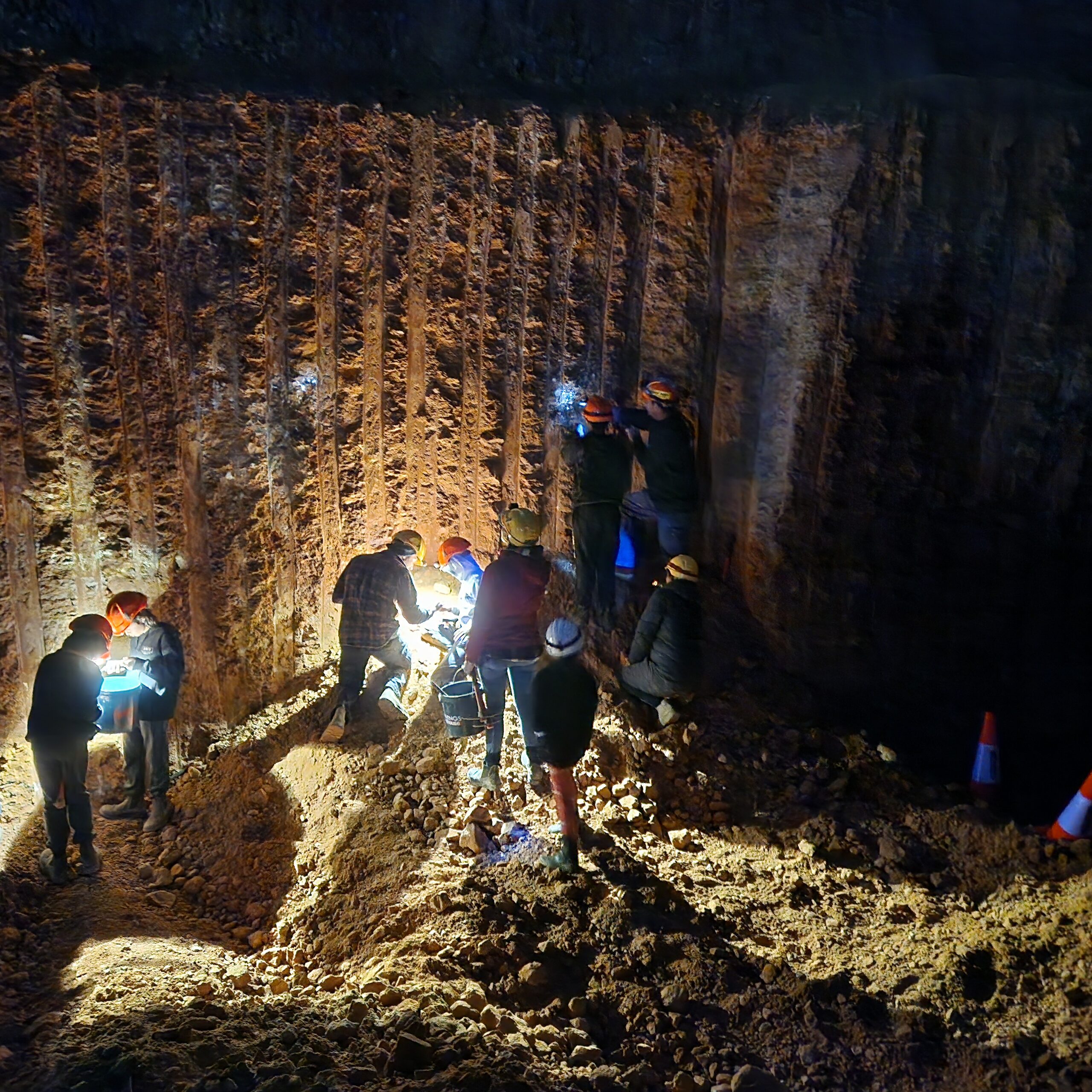 Guests on the night dig working a lit mine face with headlamps and buckets.