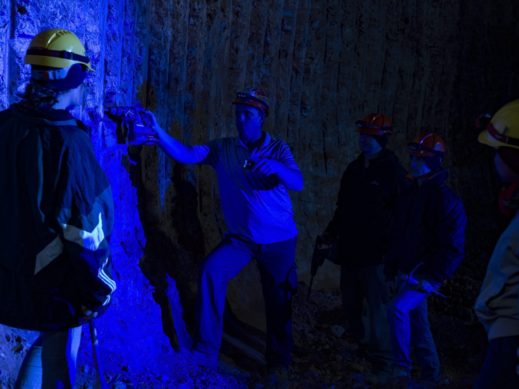 Dan and helmeted guests at the mine face under UV torchlight, the drive lit deep blue.